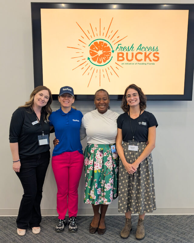Four women from Feeding Tampa Bay and Florida Nutrition Education stand in front of a Fresh Access Bucks screen.