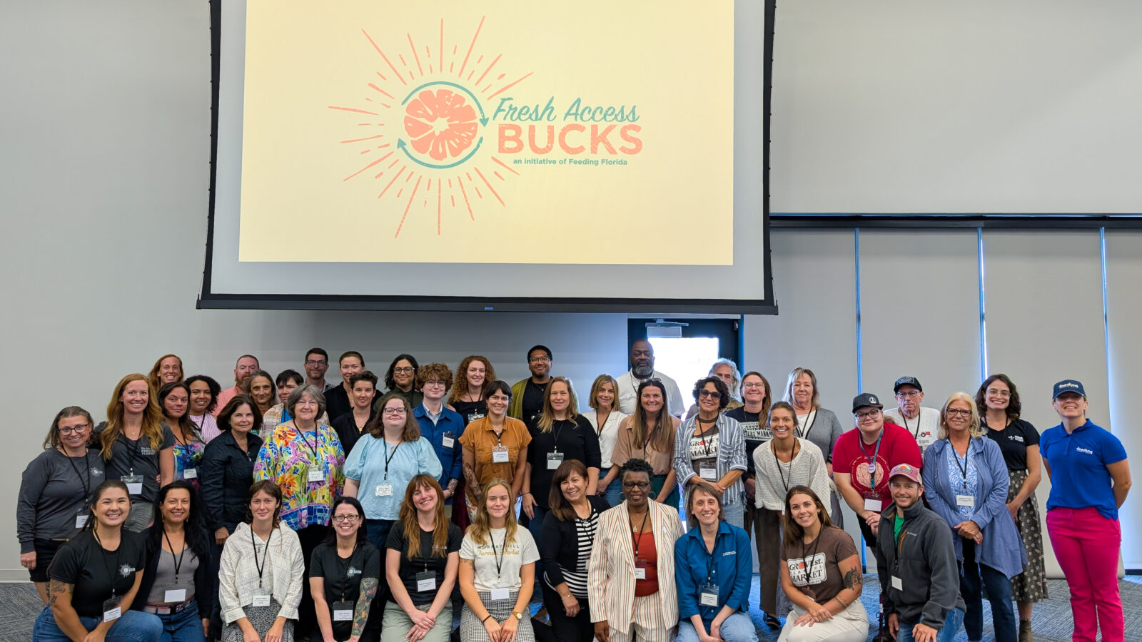 A large group of people smiling at the camera in front of a projector screen displaying “Fresh Access Bucks.” These are all the attendees of the Fresh Access Bucks Annual Convening.