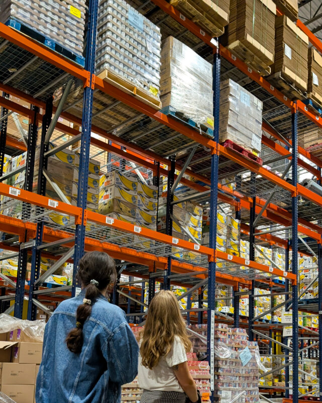 Two people look up at towering shelves stocked with food in a large warehouse.