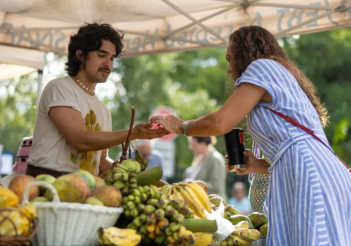 Person buying fruit from a vendor at an outdoor market stall under a tent.